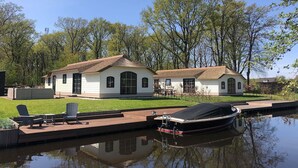 Une maison avec un quai et un bateau, entourée d’arbres et bordée par une étendue d’eau calme.
