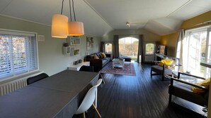 A modern living room with a dining area, large windows, and a view of the outdoors.