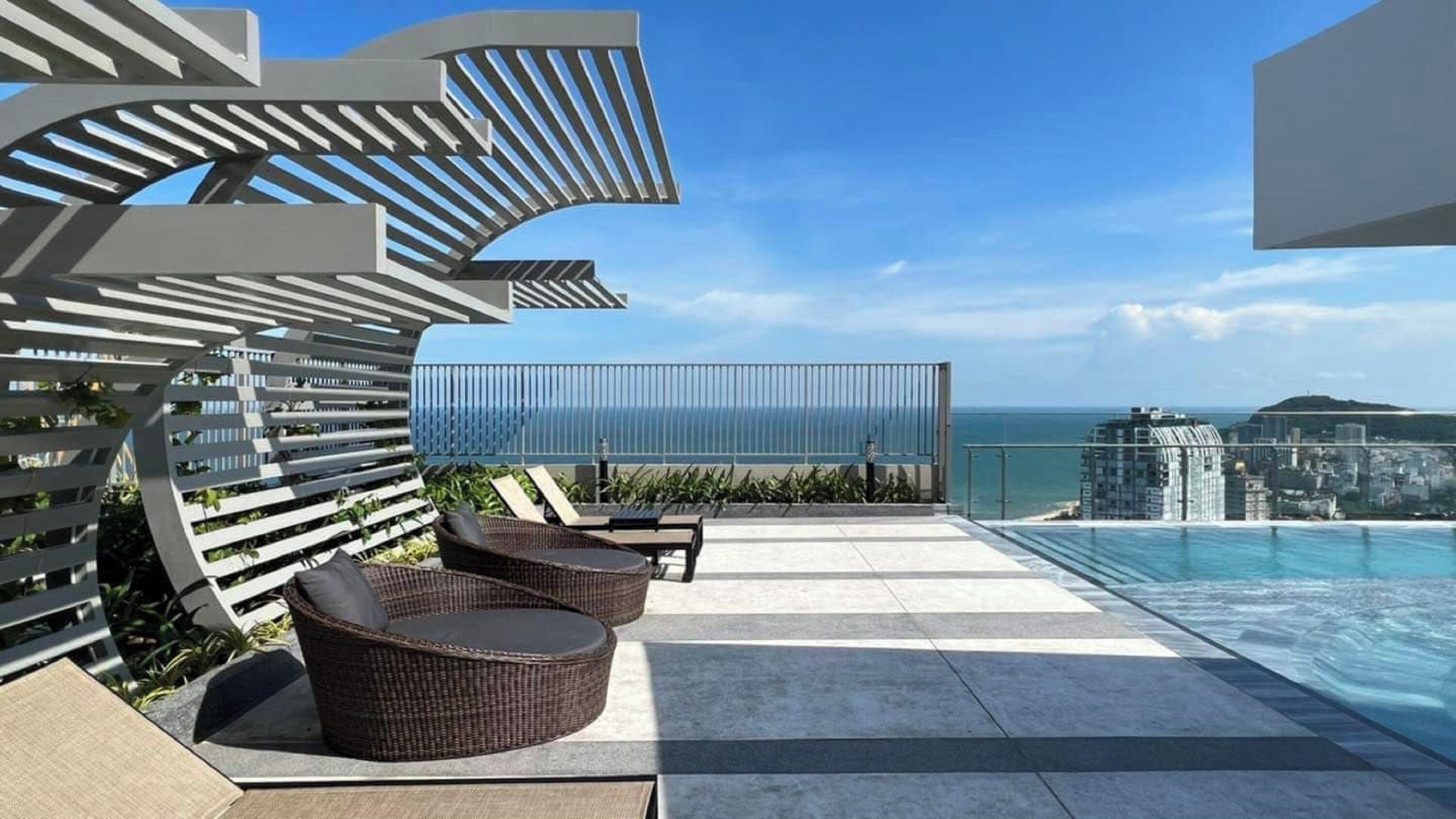 A rooftop terrace with a pool, seating area, and a view of the ocean and cityscape.