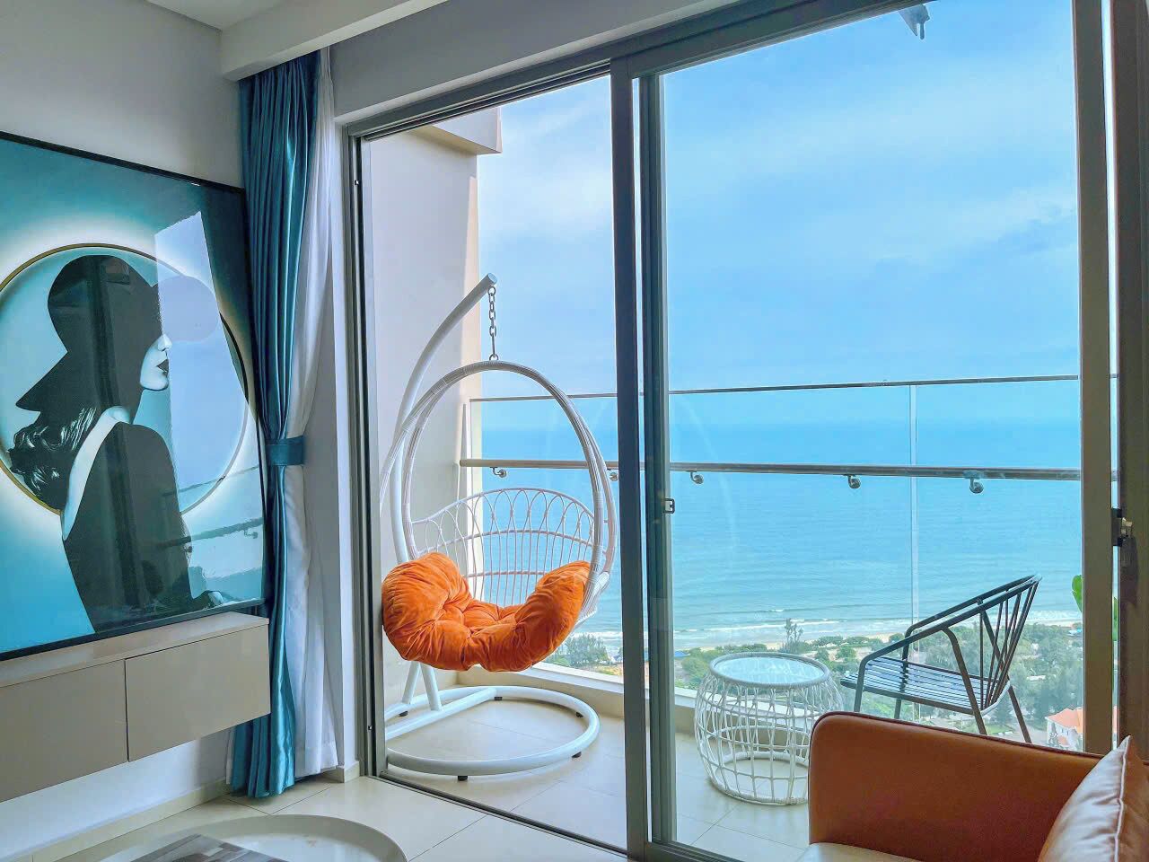 A modern hotel room with a large sliding glass door leading to a balcony with a view of the ocean.