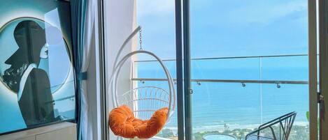 A modern hotel room with a large sliding glass door leading to a balcony with a view of the ocean.