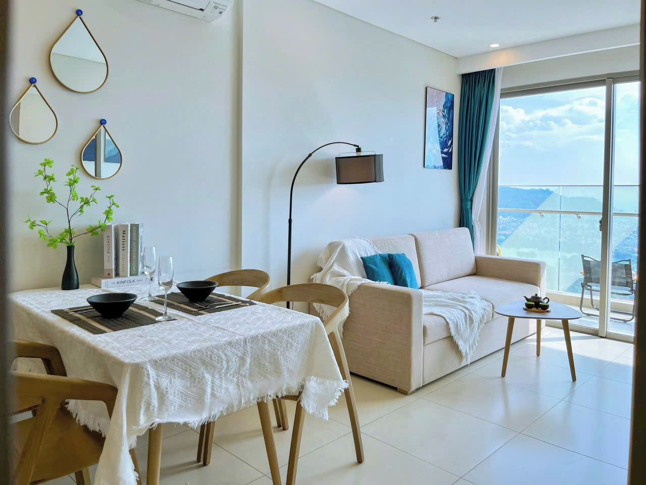 A modern living room with a dining area, a sofa, a coffee table, and a balcony with a view.