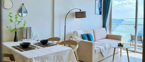 A modern living room with a dining area, a sofa, a coffee table, and a balcony with a view.