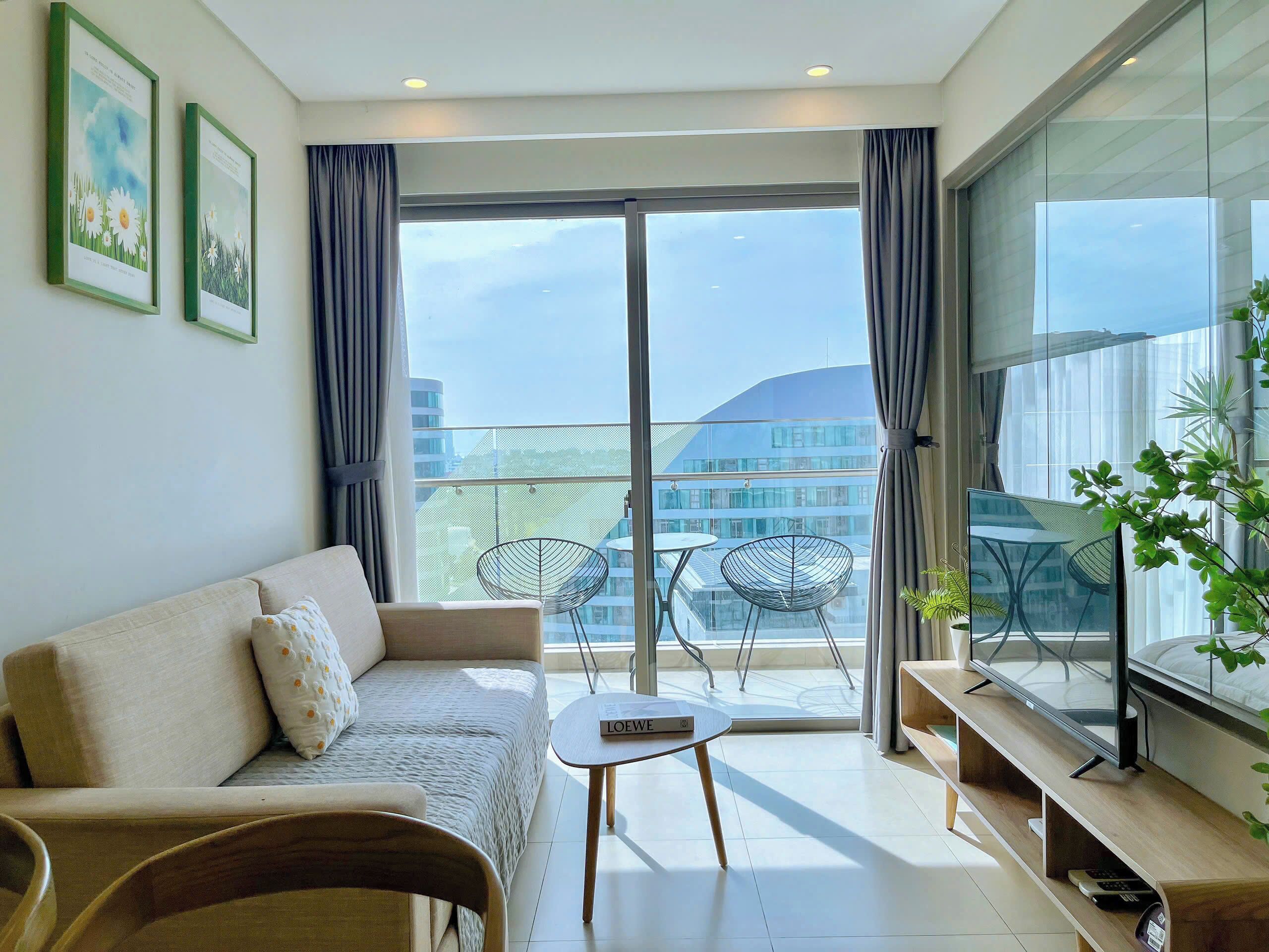 Ein modernes Wohnzimmer mit Sofa, einem kleinen Tisch, einem Fernseher auf einem Holzgestell und einem Balkon mit Sitzgelegenheiten.