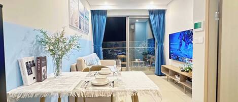 A dining area with a table set for two, a vase with flowers, and a television on the wall.