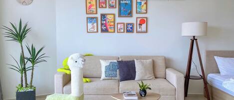 Un salon comprenant un canapé, une table basse, une lampe, une horloge murale et une rangée de tableaux encadrés.