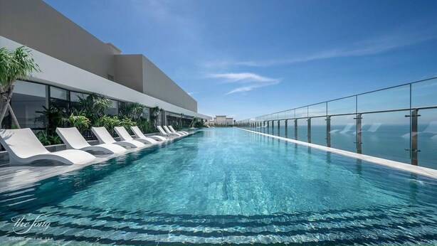 Een modern overloopzwembad met ligbedden, heldere lucht en een glazen balustrade.