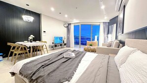 Een moderne slaapkamer met een groot bed, een eethoek, een televisie en een balkon met uitzicht over de stad.