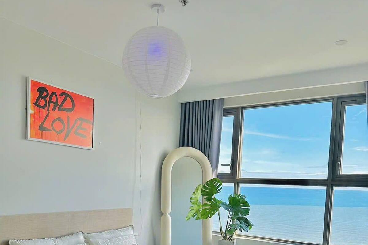 Un dormitorio con una cama grande, vistas al mar, un ventilador de techo y un letrero en la pared que dice 'Bad Love'.
