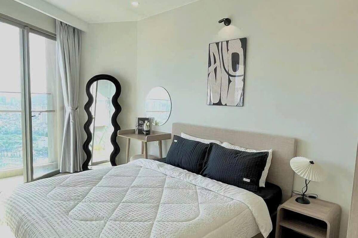 Un dormitorio moderno con una cama grande, una mesita de noche con lámpara, un espejo y una obra de arte en la pared.