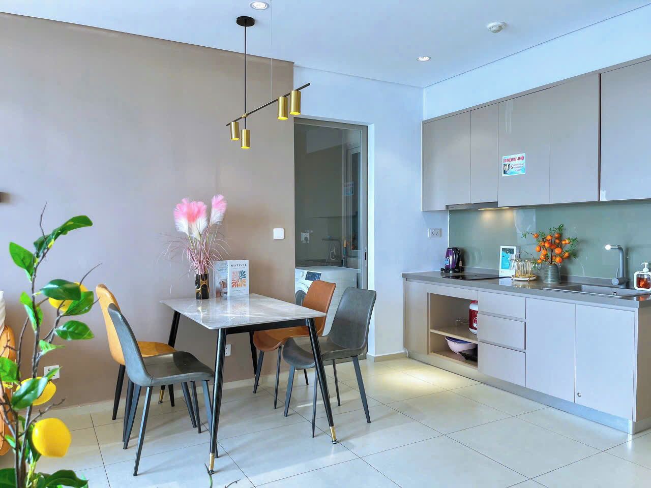 A modern kitchen with a dining area, featuring a table with chairs, a hanging light fixture, and a kitchen counter with a sink and cabinets.