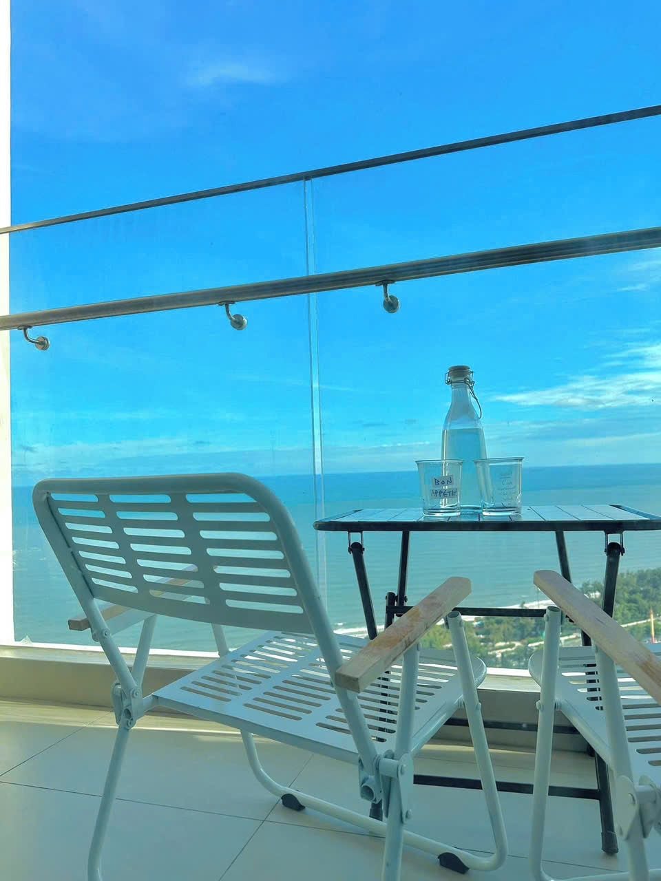 A balcony with a metal chair and table, a bottle of water, and a clear view of the sea.