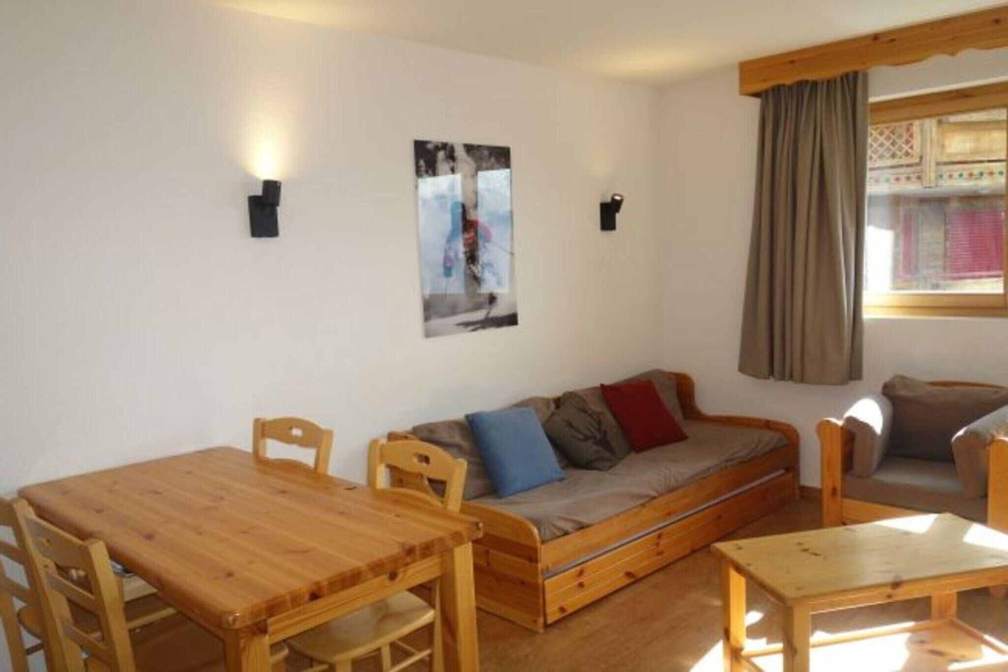 Ein gemütlicher Raum mit einem Holztisch und Stühlen, einem Sofa und einem Fenster mit Vorhängen.