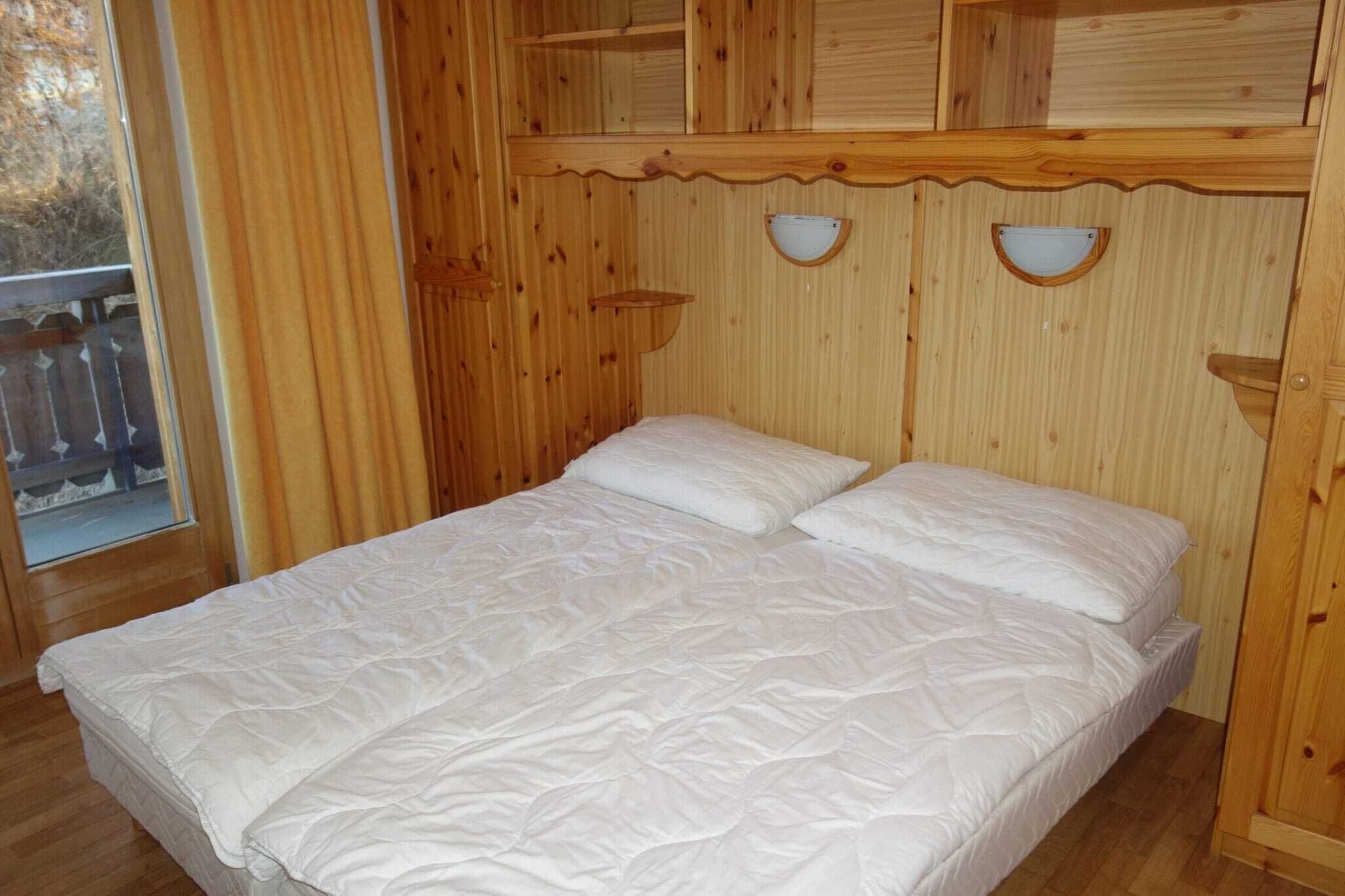 Una habitación de madera con una cama, un ventanal y una barandilla de madera en el exterior.