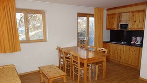 A compact room with a wooden dining table, chairs, a small wooden bench, a sofa, and a kitchenette with wooden cabinets and a microwave. - Pleasant apartment with sauna (Haute-Nendaz)