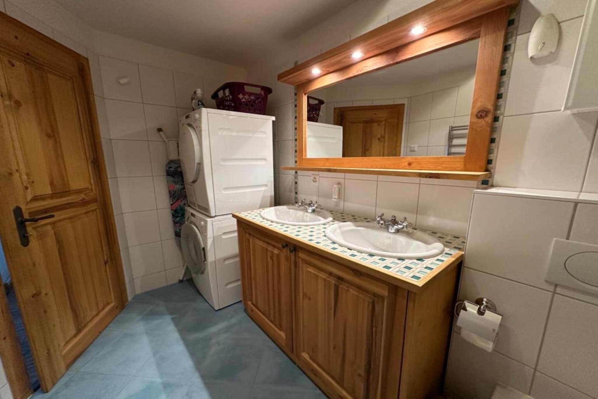 Une cuisine compacte équipée de deux éviers, de meubles en bois, d’un réfrigérateur et d’un grand miroir au-dessus du plan de travail.