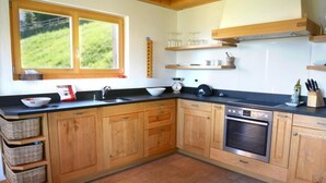 A kitchen with wooden cabinets, a built-in oven, and a window overlooking a green landscape. - Tranquil chalet with balcony (Haute-Nendaz)