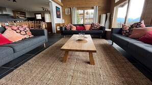 A spacious living room with a wooden coffee table, two grey sofas with patterned cushions, and a view of mountains through large windows. - Chalet in Nendaz near Ski Slopes (Haute-Nendaz)