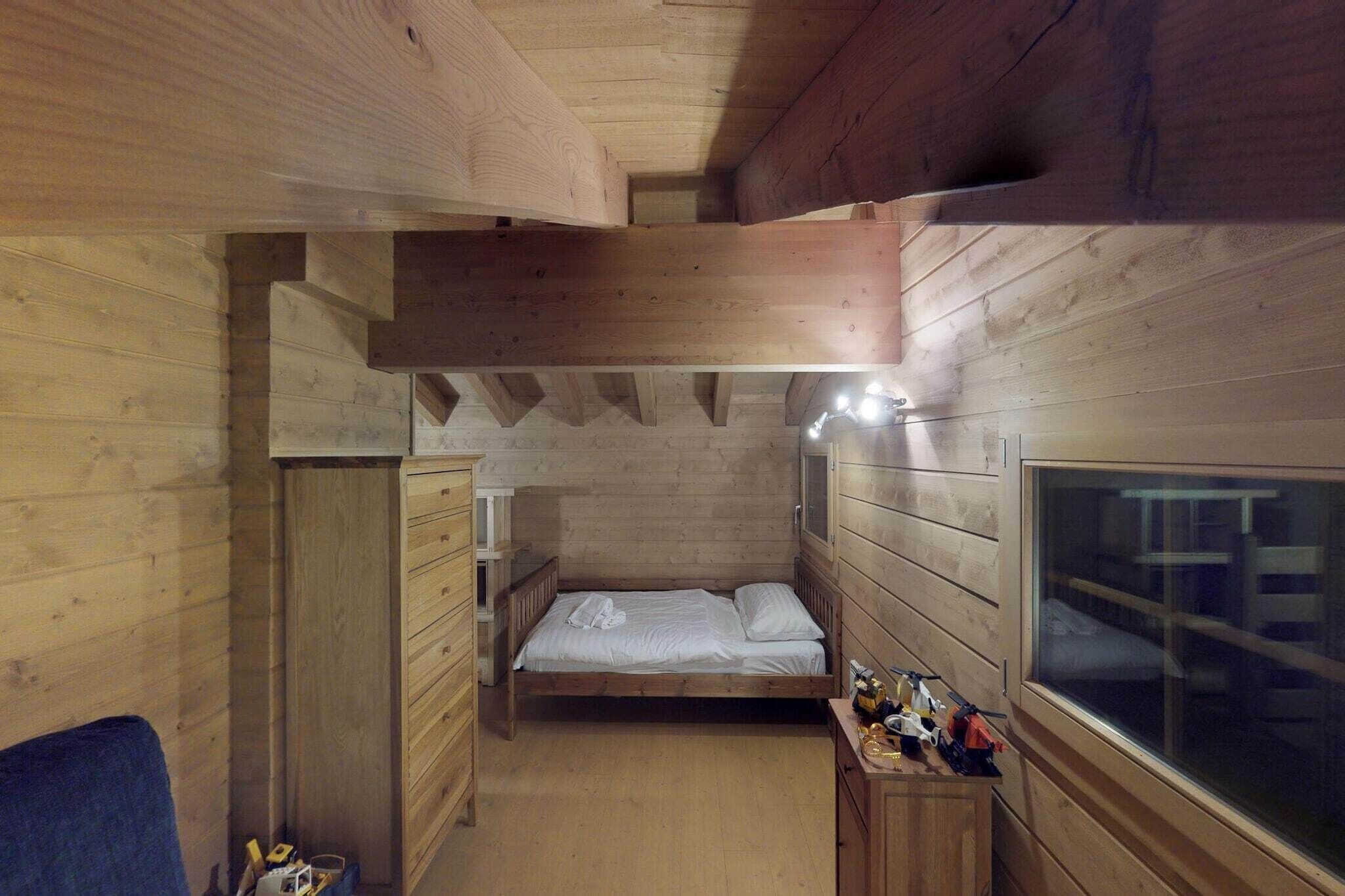 A wooden cabin room with a bed, dresser, and a window.