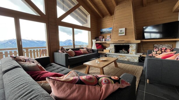 A cozy living room with a fireplace, large windows, and a view of mountains. - Chalet in Nendaz near Ski Slopes (Haute-Nendaz)