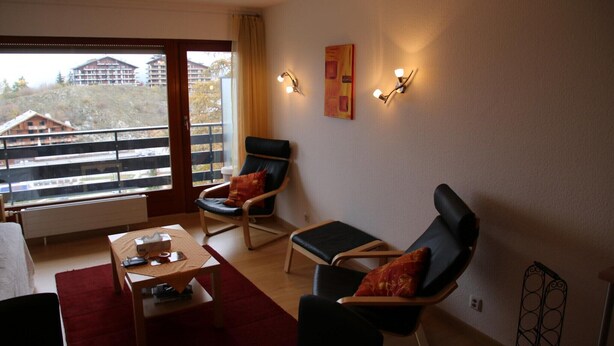 A modern living room with a balcony, two lounge chairs, a small table, and a view of buildings in the background. - Studio in Nendaz near Ski Lift (Haute-Nendaz)