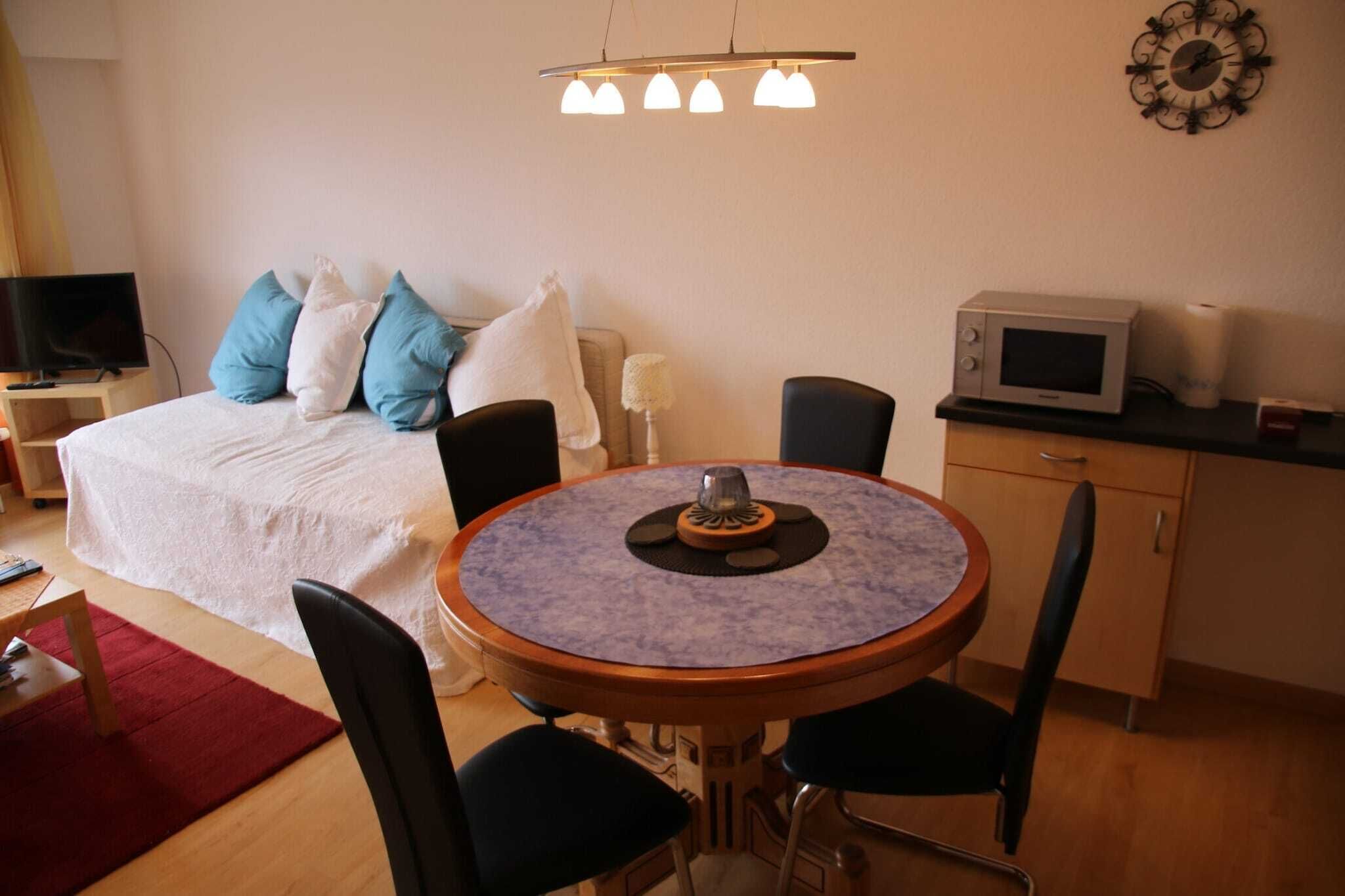 Een slaapkamer met een bed, een ronde eettafel met stoelen, een televisie, een magnetron en een klok aan de muur.