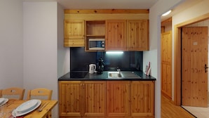 Een kleine keuken met houten kastjes, een zwart aanrechtblad en voorzieningen zoals een magnetron, waterkoker en spoelbak.