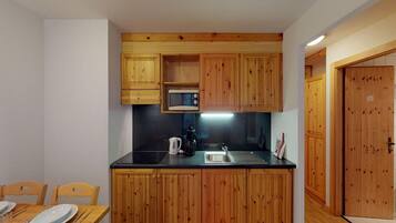 Cocina compacta con armarios de madera, encimera negra y servicios básicos como microondas, hervidor y pileta.