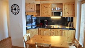 Une cuisine avec des meubles de rangement en bois, un four à micro-ondes, une machine à café et une horloge au mur.
