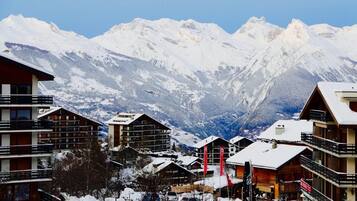 Bergresort bedekt met sneeuw, met meerdere gebouwen, waaronder een hotel met balkons en een skilift in de achtergrond.