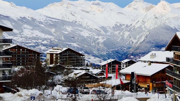 Une ville de montagne enneigée, avec des bâtiments modernes et une vue sur des sommets couverts de neige.