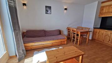 Ein gemütlicher Wohnbereich mit einer Holzdavonia, einem Esstisch und Stühlen. Es gibt eine kleine Küchenzeile mit Holzausbau und einer schwarzen Arbeitsplatte.