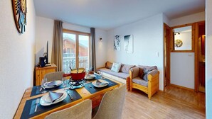 A cozy living room with a wooden dining table set for two, a sofa, and a small kitchen area with a stove. - Appealing apartment with balcony (Haute-Nendaz)