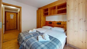A bedroom with two beds, wooden headboard, and a wooden wardrobe. - Charming apartment near ski area (Haute-Nendaz)