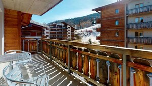 A wooden balcony with metal chairs, overlooking a snowy mountain area with buildings and a clear sky. - Charming apartment near ski area (Haute-Nendaz)