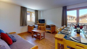 A furnished living room with a sofa, chairs, a coffee table, a TV, and a dining table set for a meal. - Modern apartment with balcony (Haute-Nendaz)