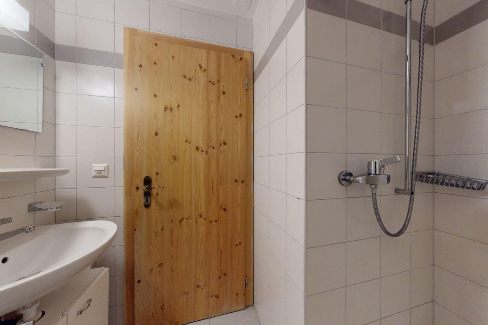 Ein Badezimmer mit Holztür, weißem Waschbecken und Dusche mit Duschbrause.