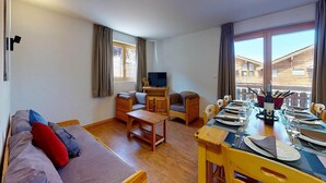 A cozy living room with a sofa, a TV, and a dining table set for two. - Modern apartment with balcony (Haute-Nendaz)