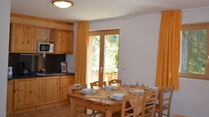 A wooden kitchen with a microwave, sink, and dining table set for four. - Amazing apartment with terrace (Haute-Nendaz)
