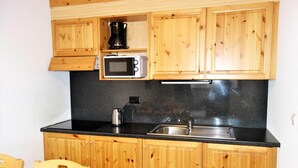Une cuisine compacte dotée de meubles en bois, d’un four à micro-ondes, d’une machine à café et d’un évier.