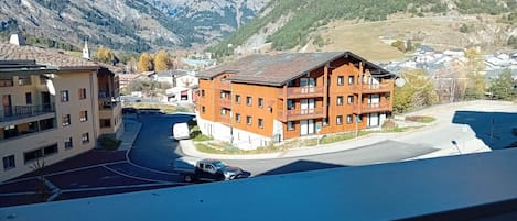 Un pueblo de montaña con un edificio rojo destacado con balcones, rodeado de casas residenciales y una iglesia.