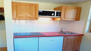 Een kleine keuken met houten kastjes, een magnetron, een vaatwasser en een rood aanrecht.