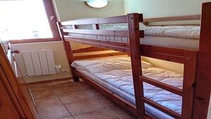 Een slaapkamer met een stapelbed, een radiator, een raam en een wandlamp.