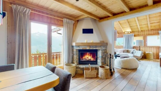 Una sala de estar acogedora con chimenea de piedra, suelo de madera y balcón con vistas a la montaña.