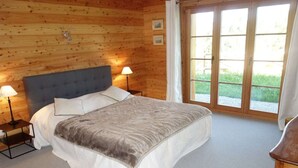 Un dormitorio con una cama grande, dos lámparas de noche, paredes de madera y un ventanal corredero que da a un jardín.