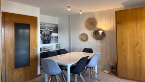 Un coin repas avec une table blanche et des chaises grises, une porte en bois et un mur orné de paniers tressés et d’un tableau encadré.