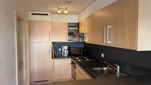 Une cuisine compacte dotée de meubles en bois, d’un plan de travail noir, d’appareils électroménagers en acier inoxydable et d’un four encastré.