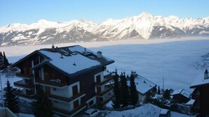 Un chalet à plusieurs étages, doté de balcons, entouré de montagnes enneigées et offrant une vue sur un lac.
