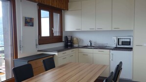 A kitchen with a wooden table, chairs, a microwave, and a coffee maker. - Pleasant apartment with balcony (Veysonnaz)