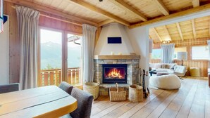 A cozy room with a stone fireplace, wooden flooring, and a balcony with a mountain view. - Beautiful chalet in Le Bouveret with garden (Les Masses)